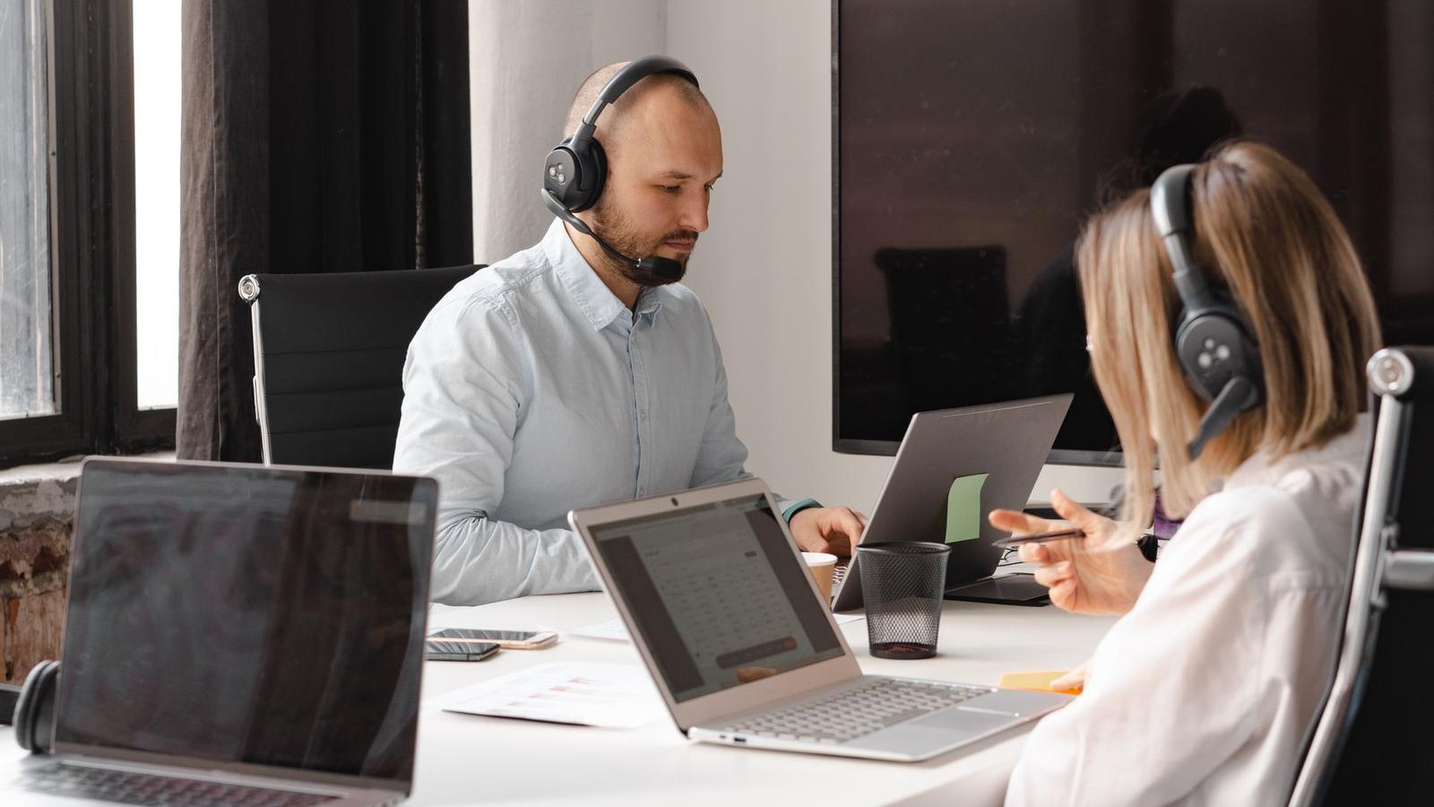 Two customer service representatives with headsets working at laptops in a dispatch office.