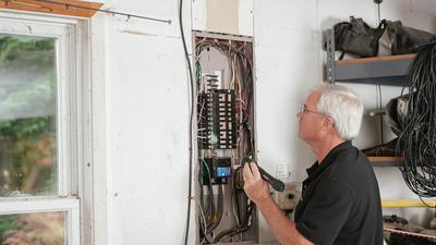 An electrician inspecting a residential fuse box with a multimeter.