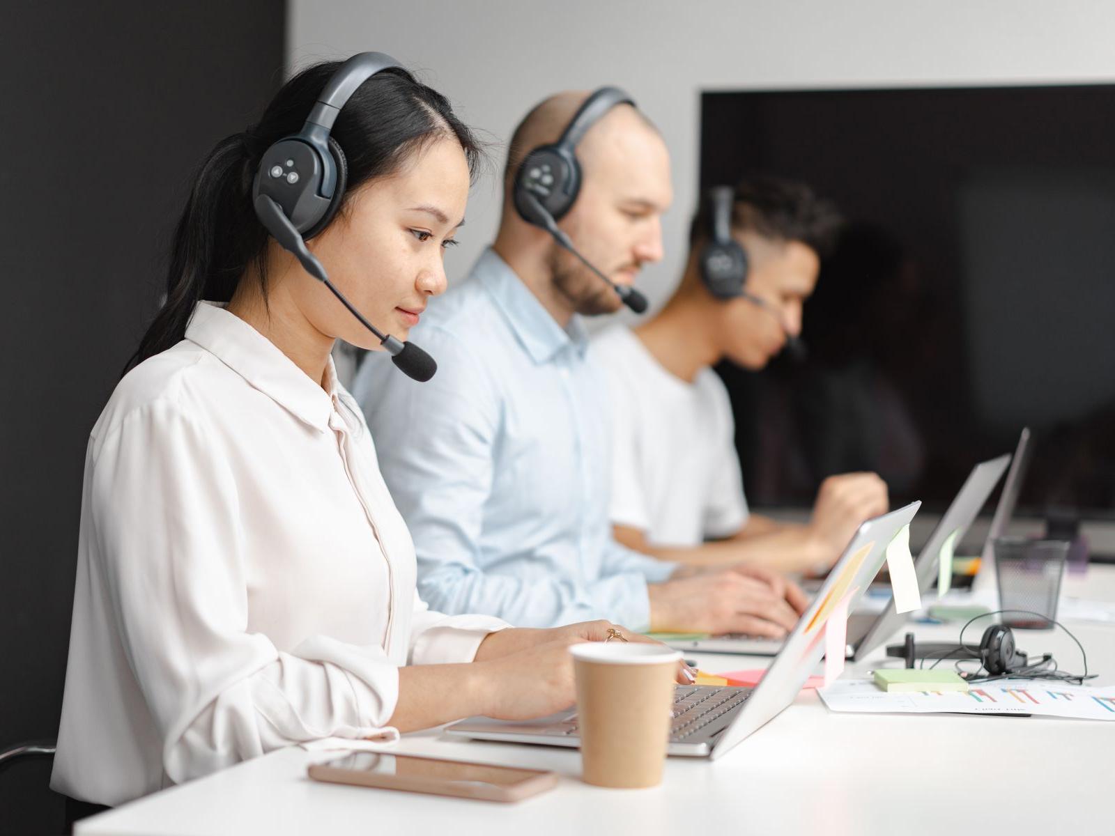 Customer service representatives wearing headsets, working an inbound call queue at a shared desk.