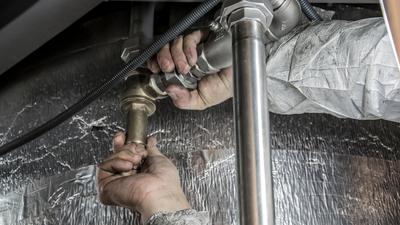 A plumber installing pipe fittings underneath a sink.