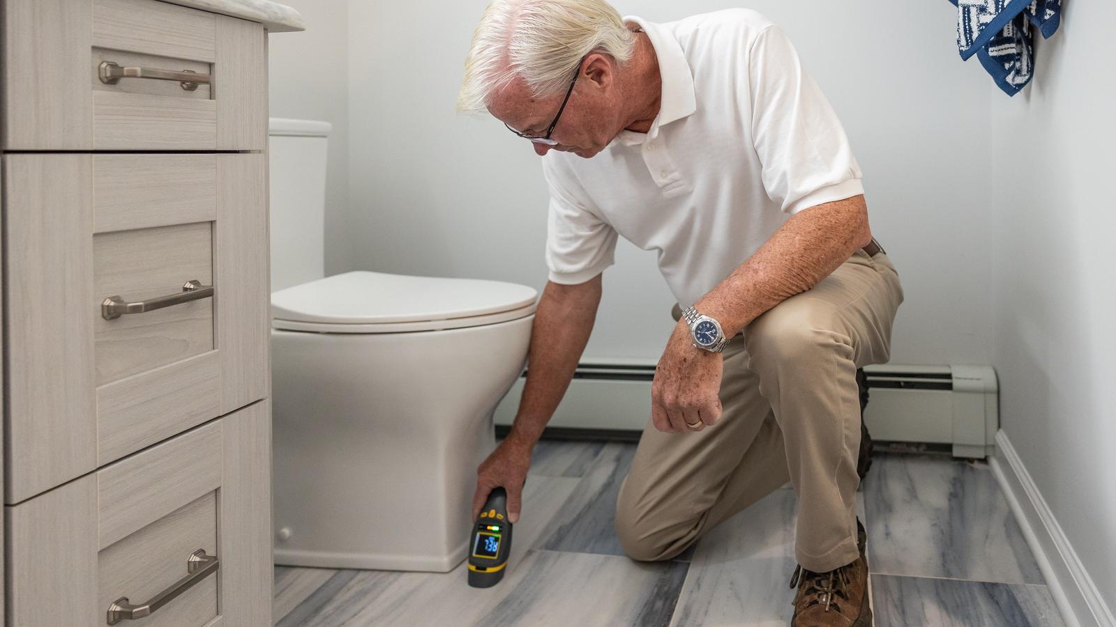 An inspector kneeling to check a bathroom for moisture damage with a handheld meter.