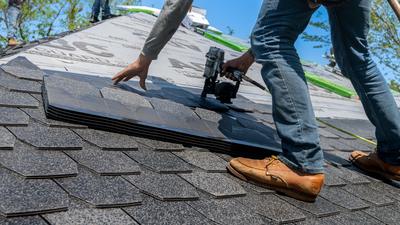 A roofer installing shingles on a new roof with a nail gun.