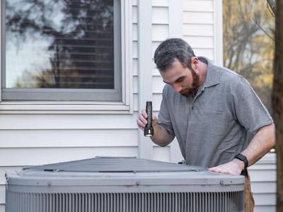 A service technician inspecting a residential outdoor condensing unit.